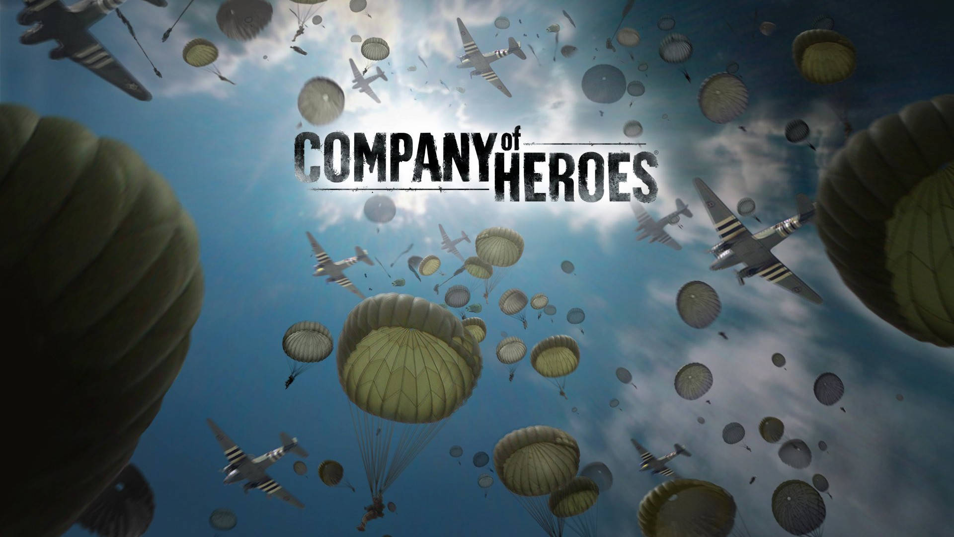 英雄連隊傘兵與飛機 壁紙 — 傘兵在陰雲密佈的天空中降落，而復古軍用飛機在頭頂飛過，構成戲劇性的戰爭場景。