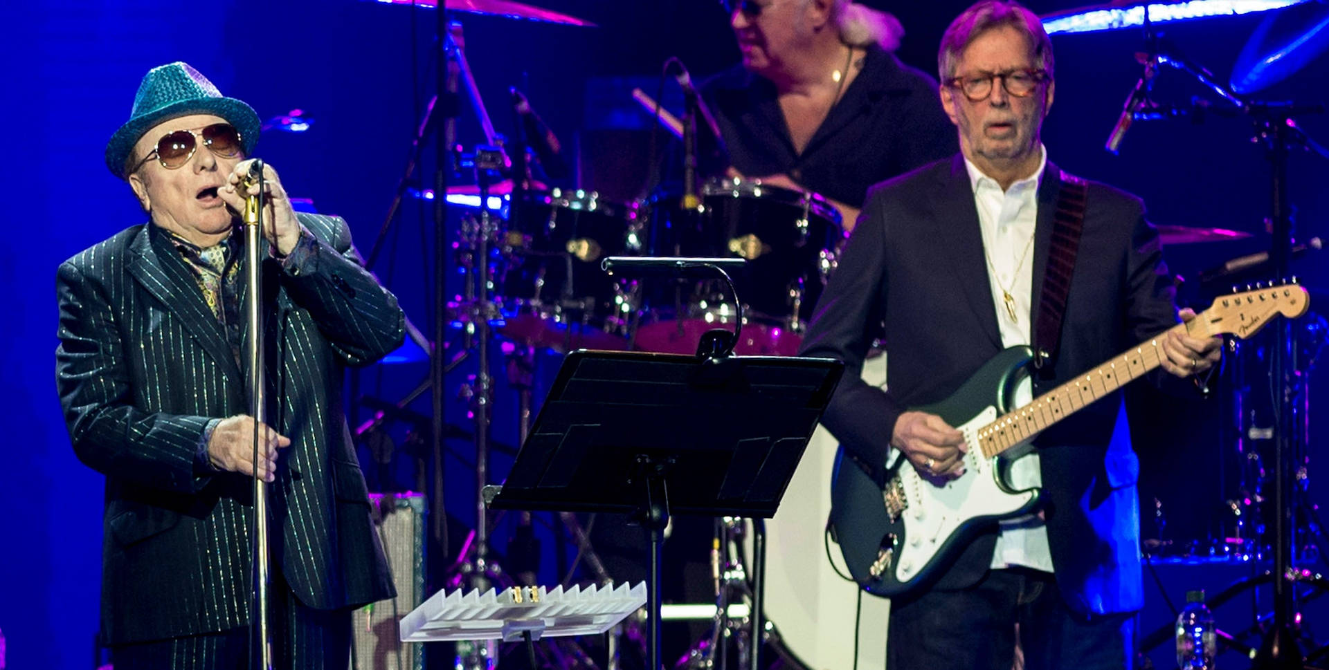 Elvis Costello 與結他手在藍色燈光下於舞台上唱歌。
