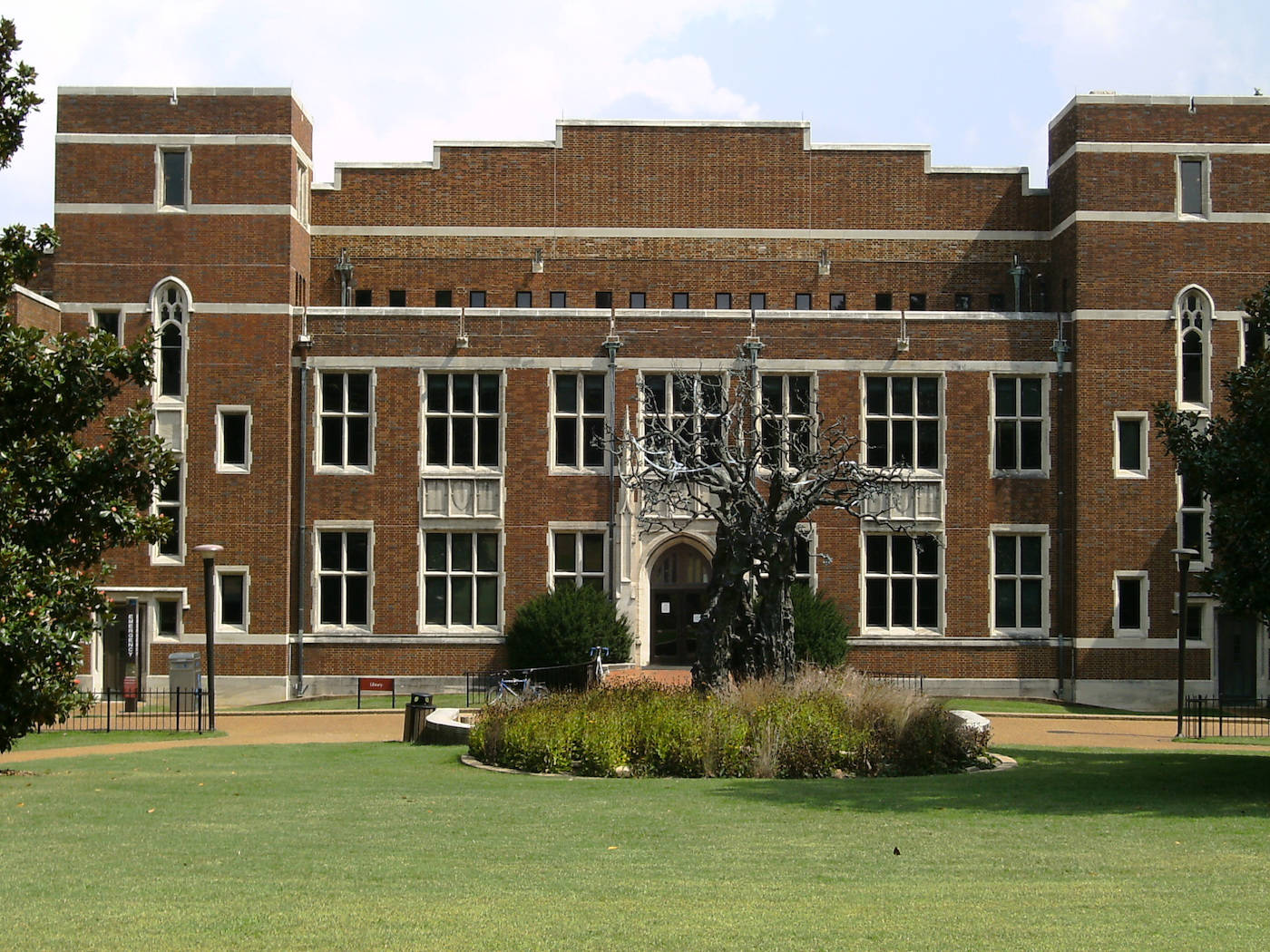大型磚造大學建築，擁有拱形窗戶和中央入口，周圍環繞著綠色草坪和樹木。
