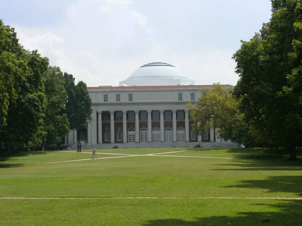 一個晴朗的日子裡，一座大型圓頂大學建築被綠色草坪和樹木環繞。