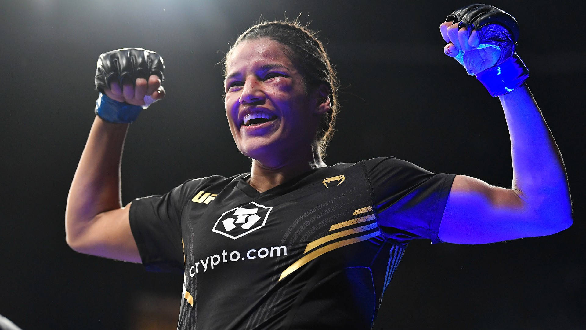茱莉安娜·佩納慶祝勝利 壁紙 — 一位女性MMA拳手在戲劇性的藍色競技場燈光下舉起拳頭慶祝勝利。