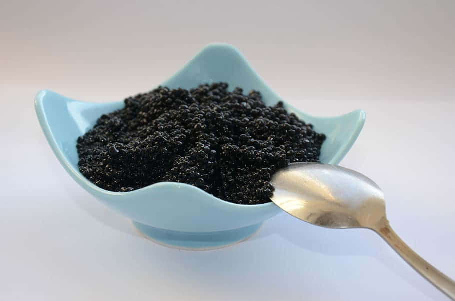 茶匙上的魚子醬 壁紙 — 一個淺藍色扇貝形碗盛載著閃閃發光的黑魚子醬，旁邊有一把銀匙放在白色表面上。