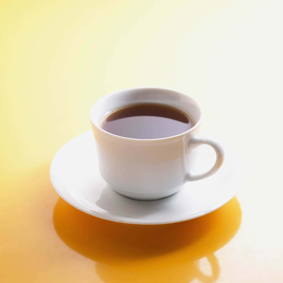 茶杯放在小碟子上圖 壁紙 — 一個純白咖啡杯盛載著深色咖啡，放在相配的碟子上，背景是溫暖的黃色漸變。