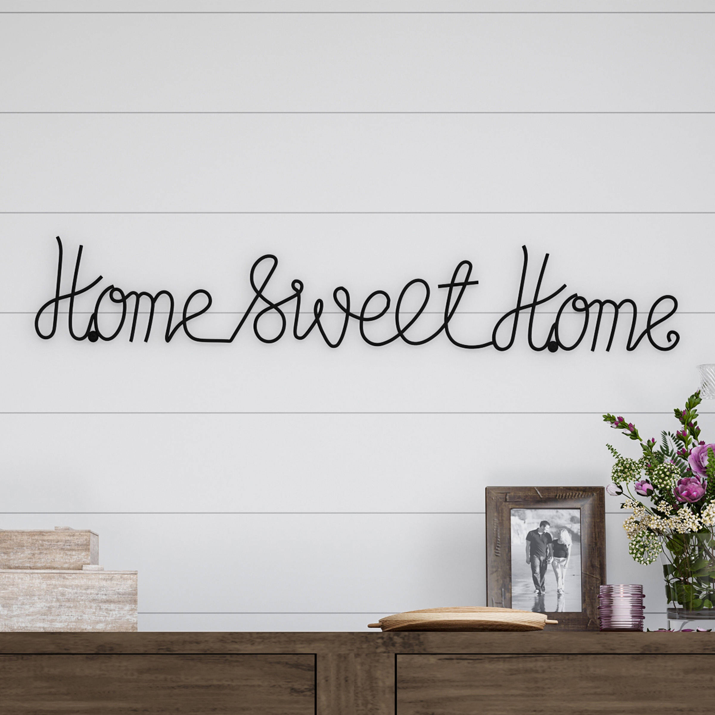 草書家園甜蜜 壁紙 — 一個黑色鐵線 'Home Sweet Home' 標牌掛在白色船艙牆上，下方木質矮櫃上放有相框和花卉擺設。