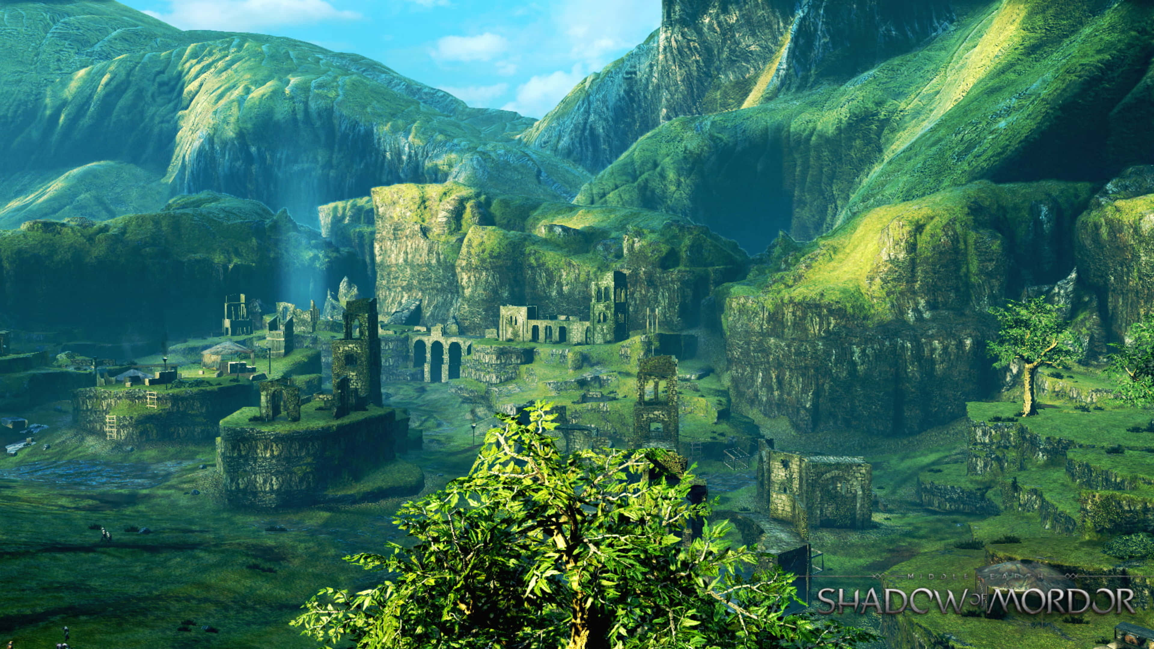 荒廢之城 4K《魔多之影》背景 壁紙 — 古代石廢墟坐落於蒼翠山谷中，四周環繞著高聳的山脈，天空湛藍明亮。