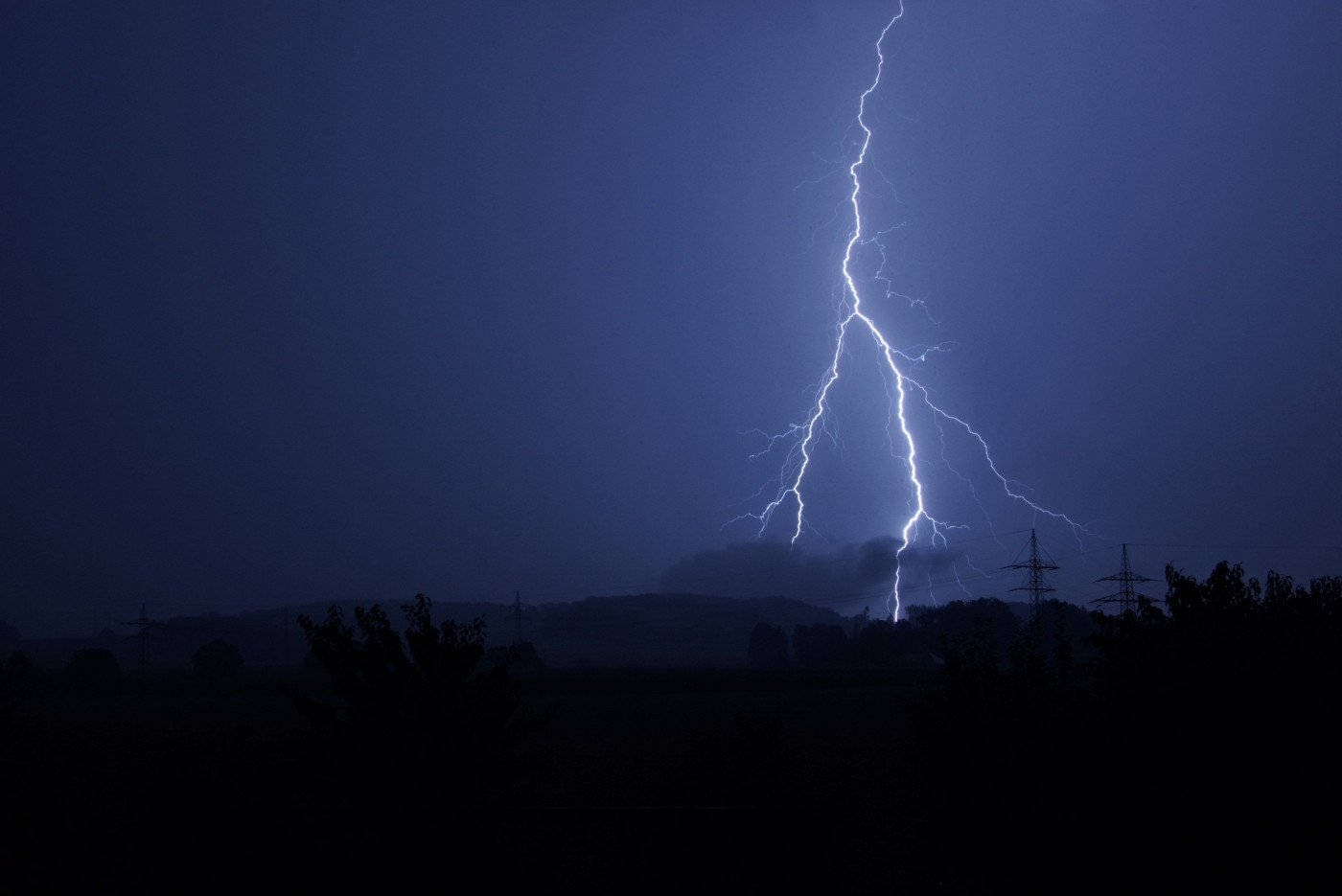 明亮的閃電照亮了黑暗的夜空，映襯出山丘和電線的剪影。