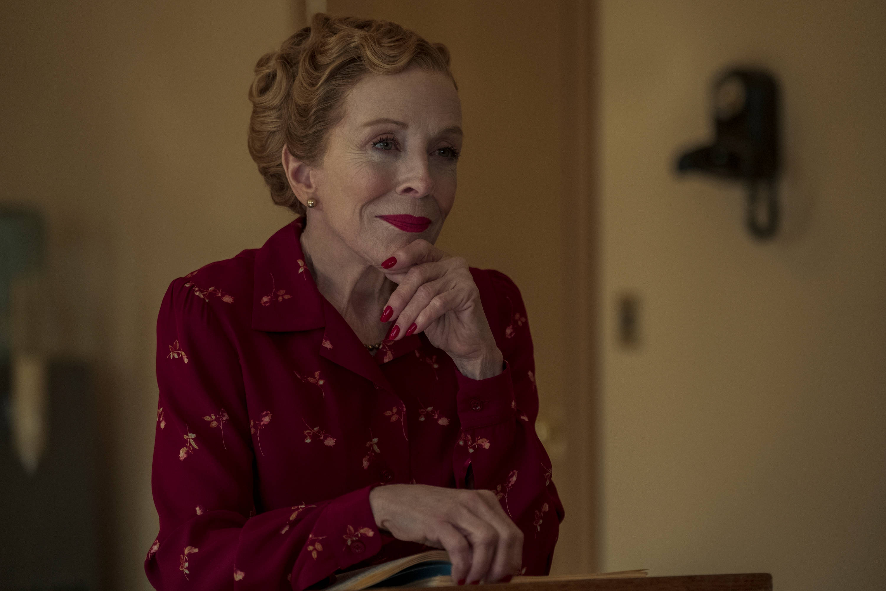 荷蘭·泰勒出演Netflix《好萊塢》劇集 壁紙 — 一位身穿紅色花卉圖案襯衫的女性，在溫暖光線的房間裡，用手托著下巴，表情若有所思。