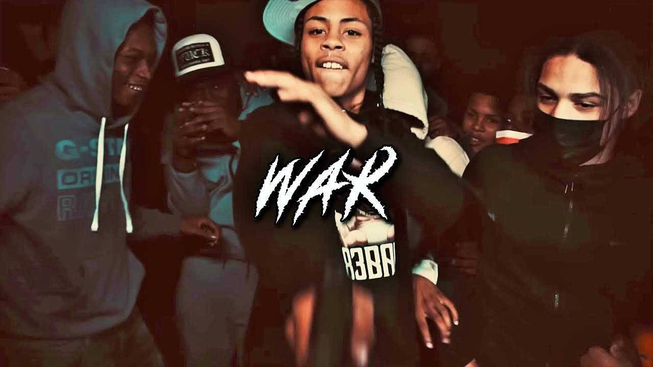 一位年輕人向前指著，帶有「WAR」圖案，在黑暗的室內環境中被人群包圍。