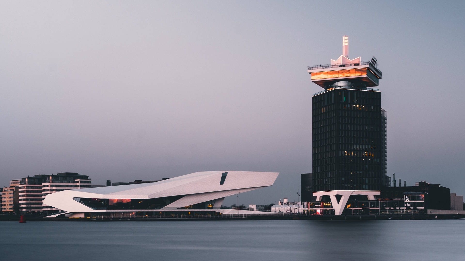 荷蘭現代城市風景 壁紙 — 現代建築在黃昏時分在平靜的水邊柔和發光，營造出時尚的城市海濱場景。