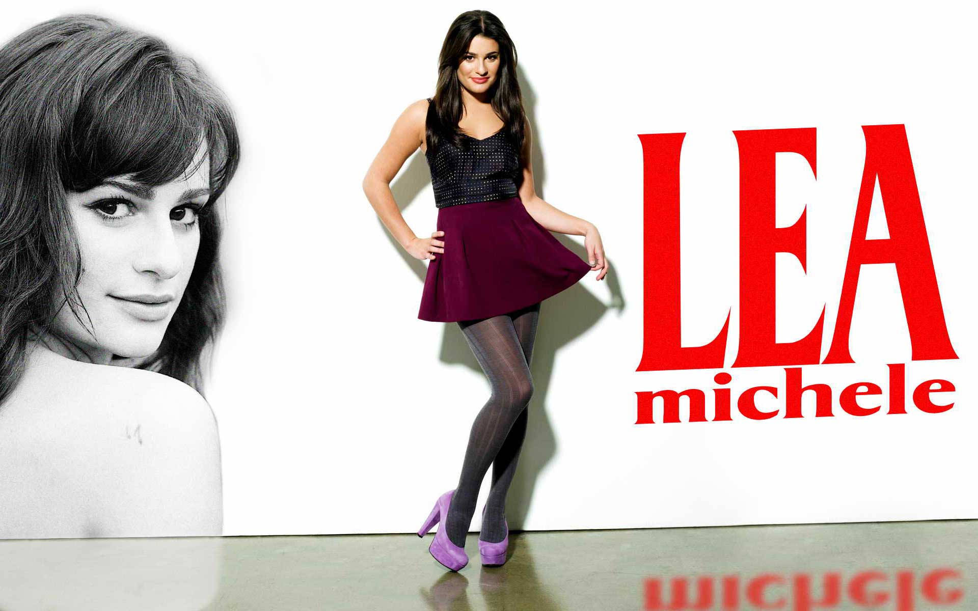 莉亞·米雪兒黑色上衣酒紅色裙裝 壁紙 — Lea Michele 自信地擺姿勢，身穿黑色上衣和紫色裙子，背景為白色，她的名字以粗體紅色字母呈現。
