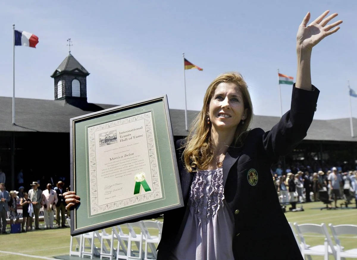 莫妮卡·塞萊斯手持獎狀 壁紙 — Monica Seles 在陽光明媚的網球場上高興地揮舞著她的國際網球名人堂獎牌。