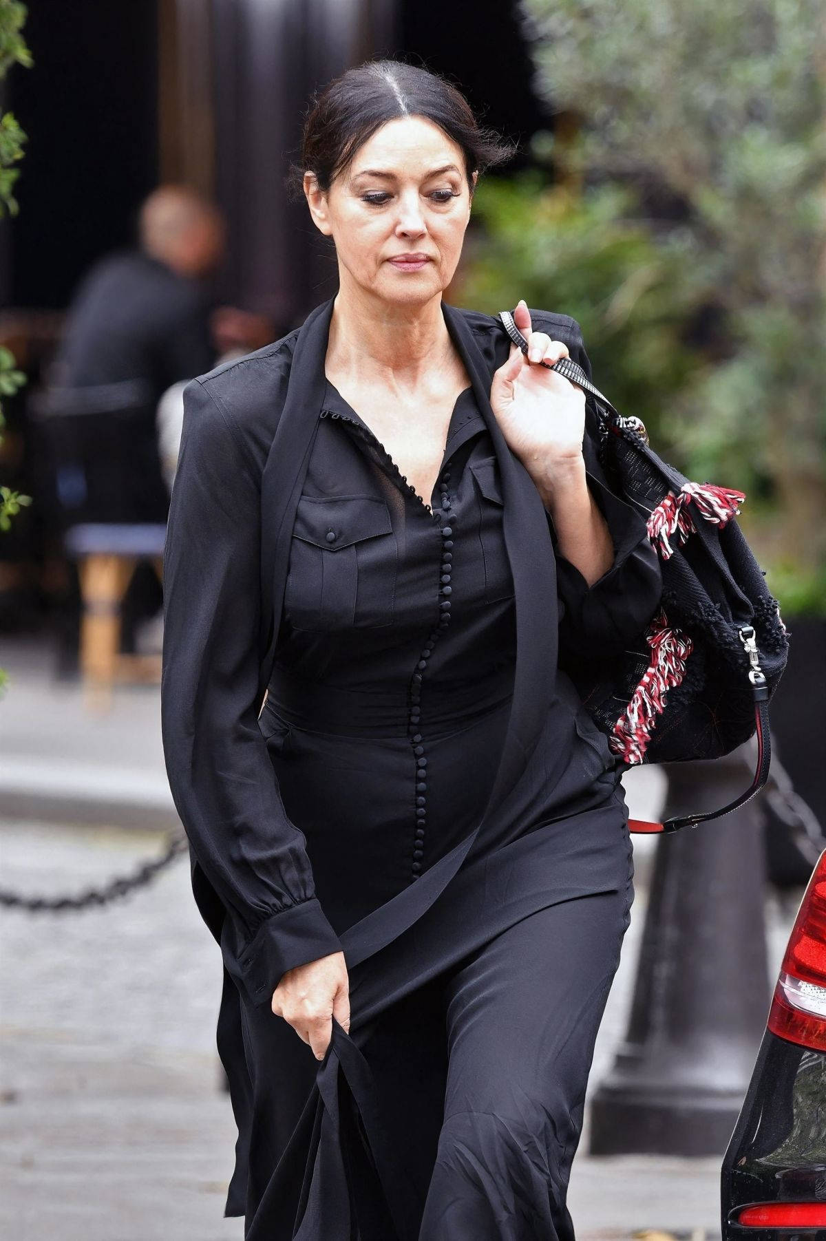 莫妮卡·貝魯奇休閒街拍 壁紙 — 一位身穿黑色服裝的女性自信地走在城市街道上，手持一個圖案手袋。