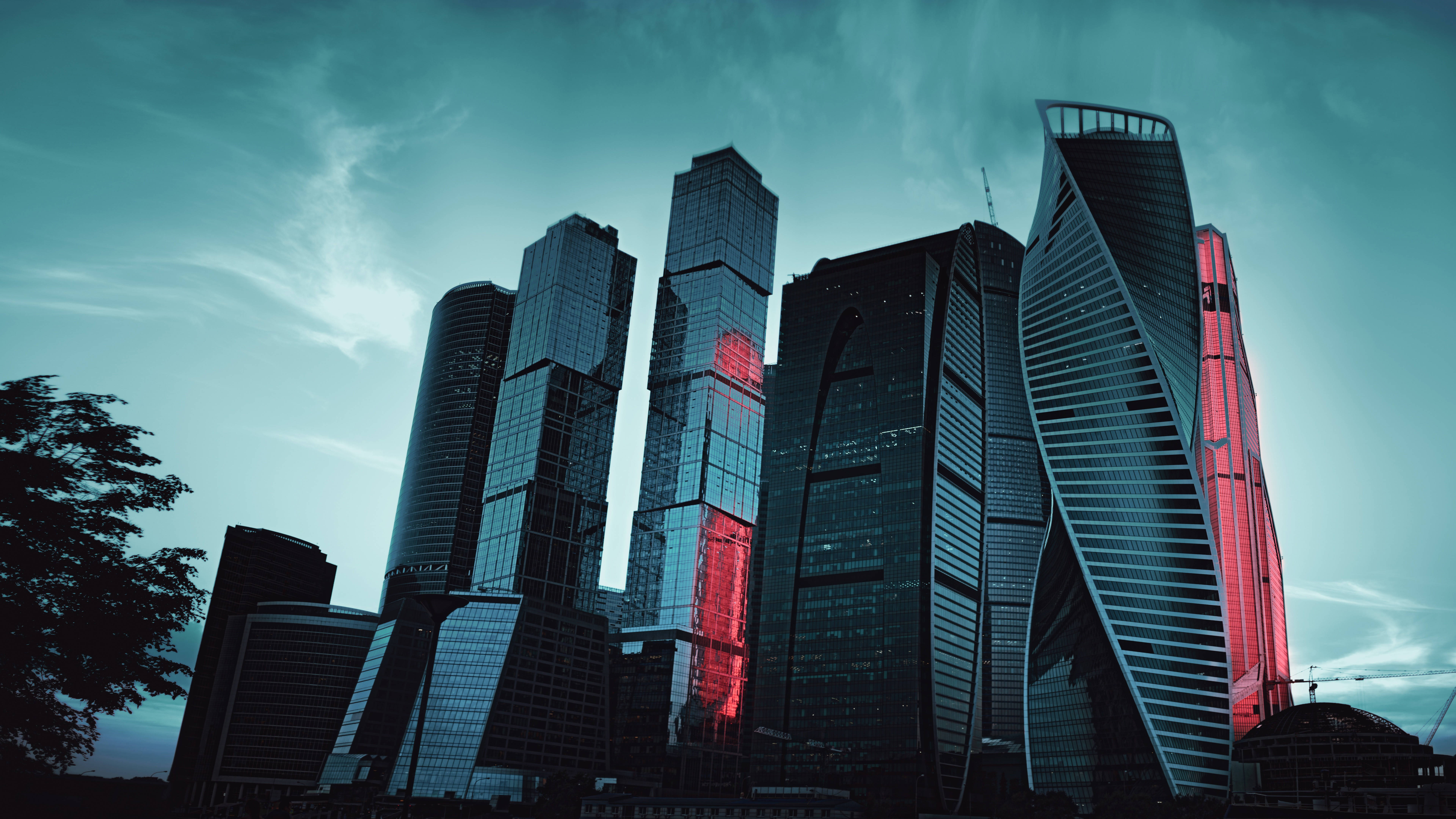 莫斯科俄羅斯濾鏡城市風景 壁紙 — 高聳的玻璃摩天大樓刺穿青綠色的暮色天空，大膽的紅色照明點綴在黑暗的外牆上閃耀。