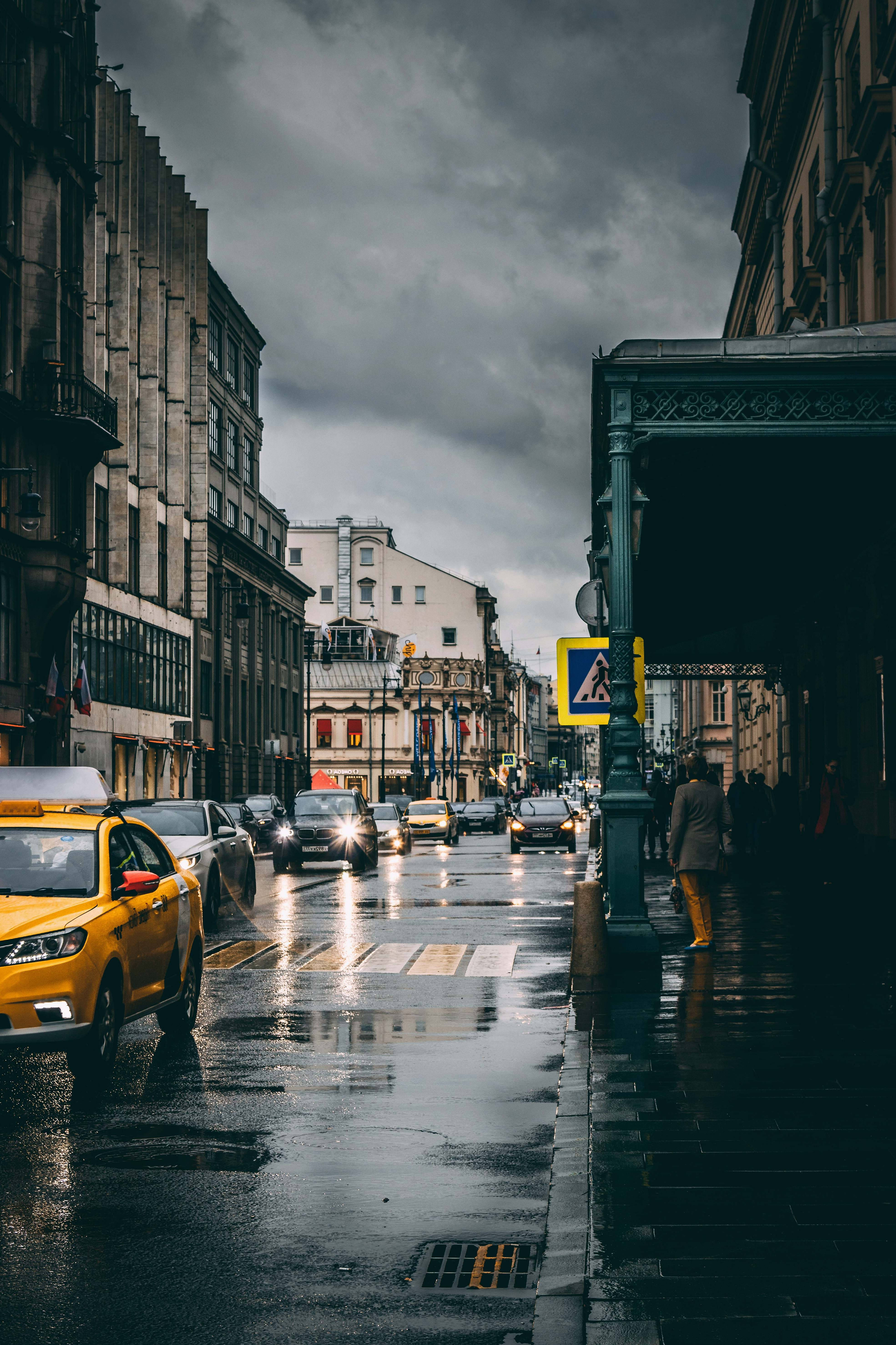莫斯科俄羅斯街景 壁紙 — 一條雨中的城市街道，濕漉漉的路面在陰暗多雲的天空下反射著車頭燈。