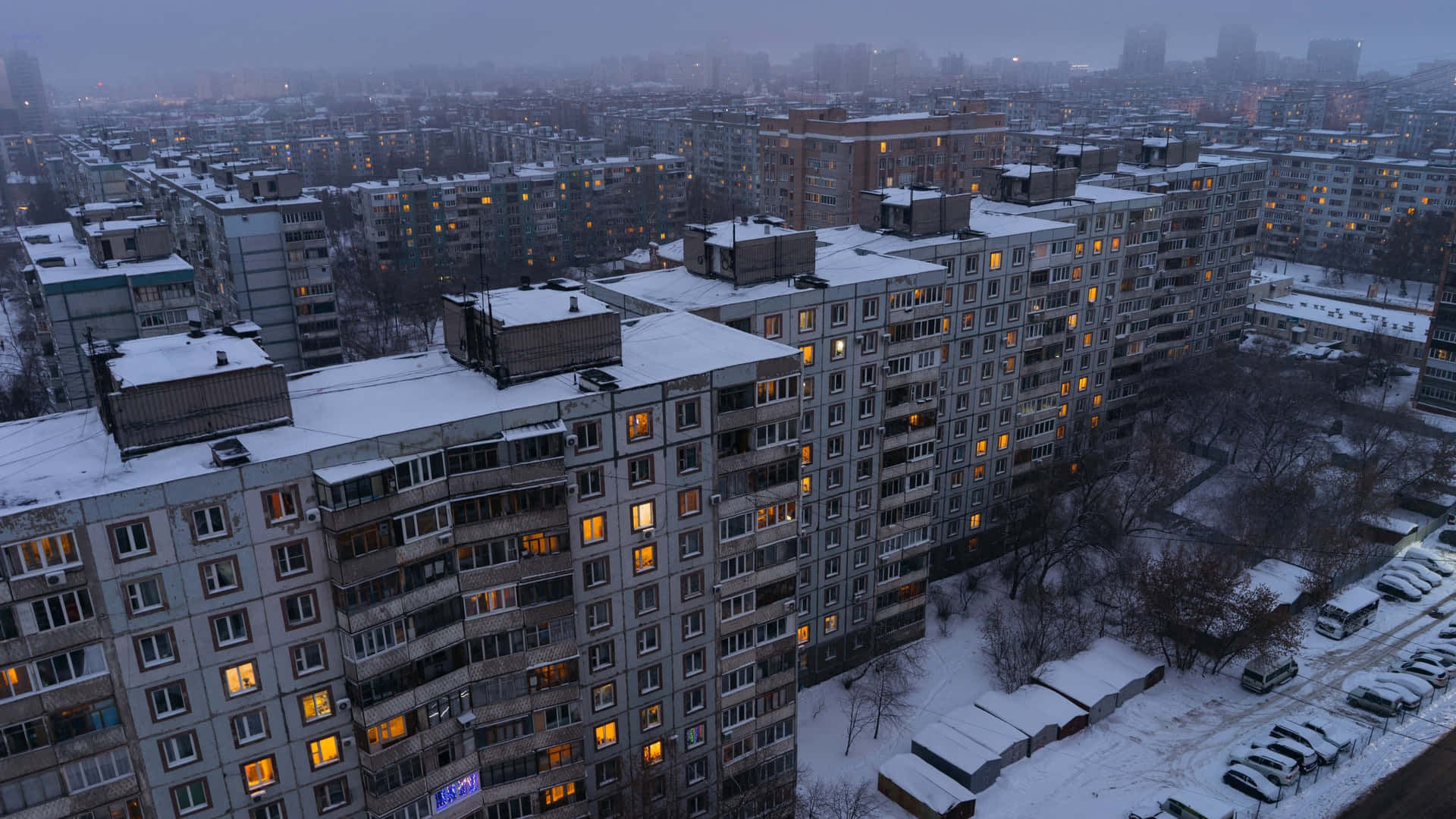 被雪覆蓋的公寓建築，窗戶在冬日城市景觀的暮色中閃爍著光芒。