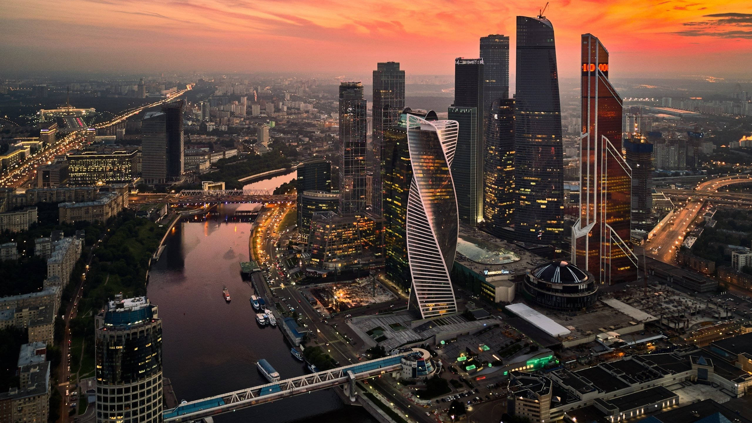 莫斯科摩天大樓水銀城塔 壁紙 — 現代城市天際線的鳥瞰圖，夕陽西下，摩天大樓閃閃發光，河流蜿蜒穿過城市景觀。