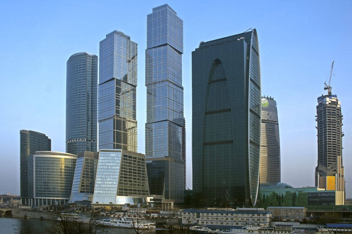 莫斯科首都城市極簡風 壁紙 — 現代玻璃摩天大樓在繁華的城市天際線中反射藍天和河上的船隻。
