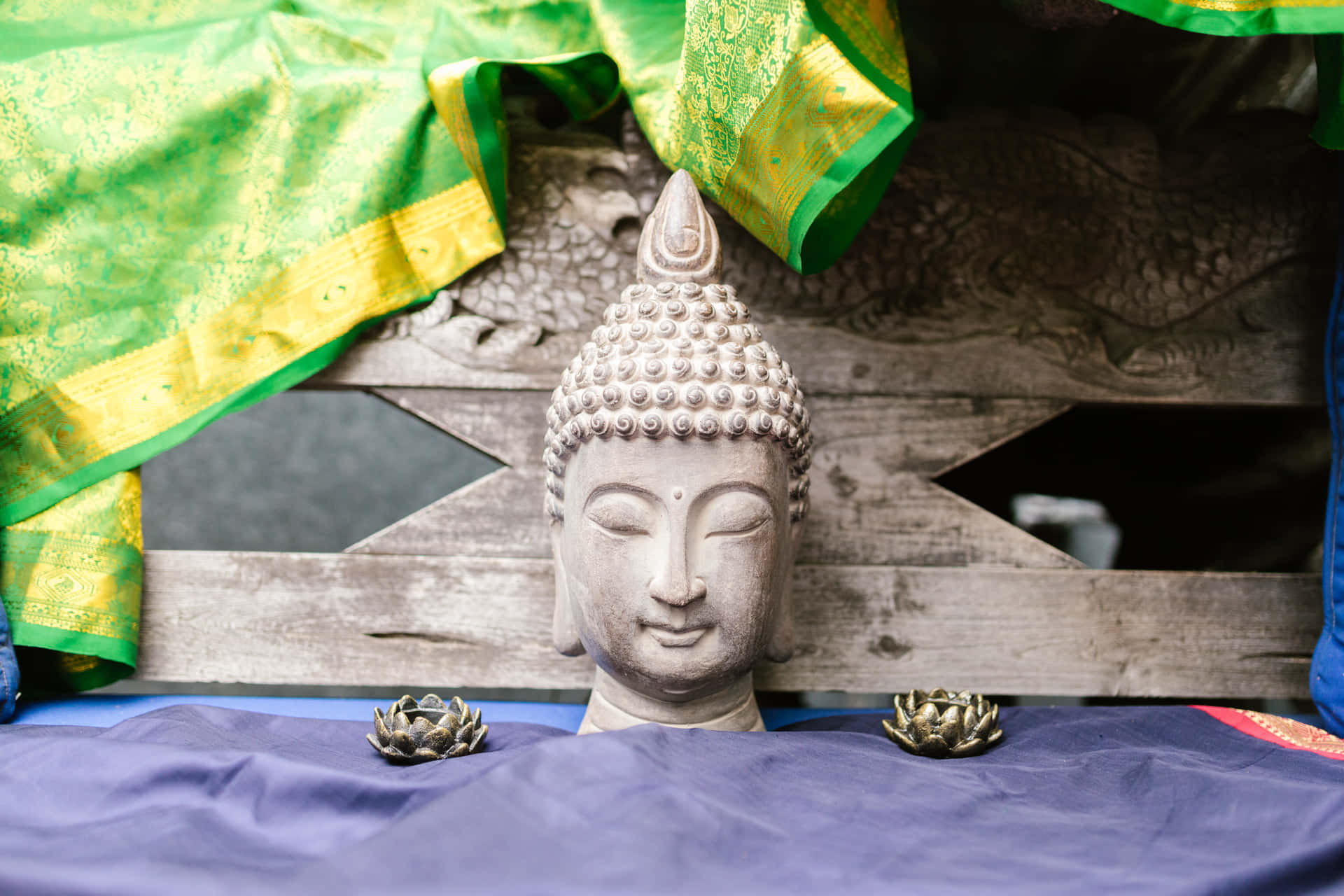 石佛頭與蓮花裝飾在紫色布上，下方有綠色和金色布料垂掛。
