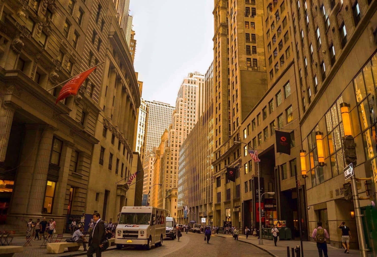 繁忙的城市街道，有高聳的石建築和行人在溫暖的夕陽光下行走。