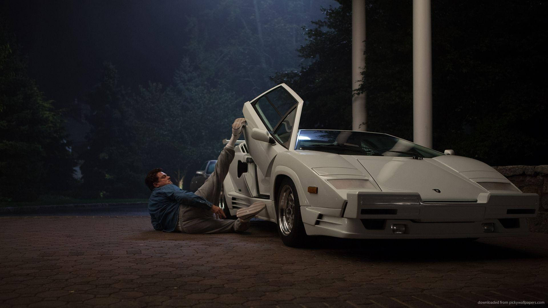 《華爾街之狼》豪華跑車 壁紙 — 一名男子在夜晚靠在一輛白色林寶堅尼Countach旁邊，其鷗翼門在戲劇性燈光下打開。