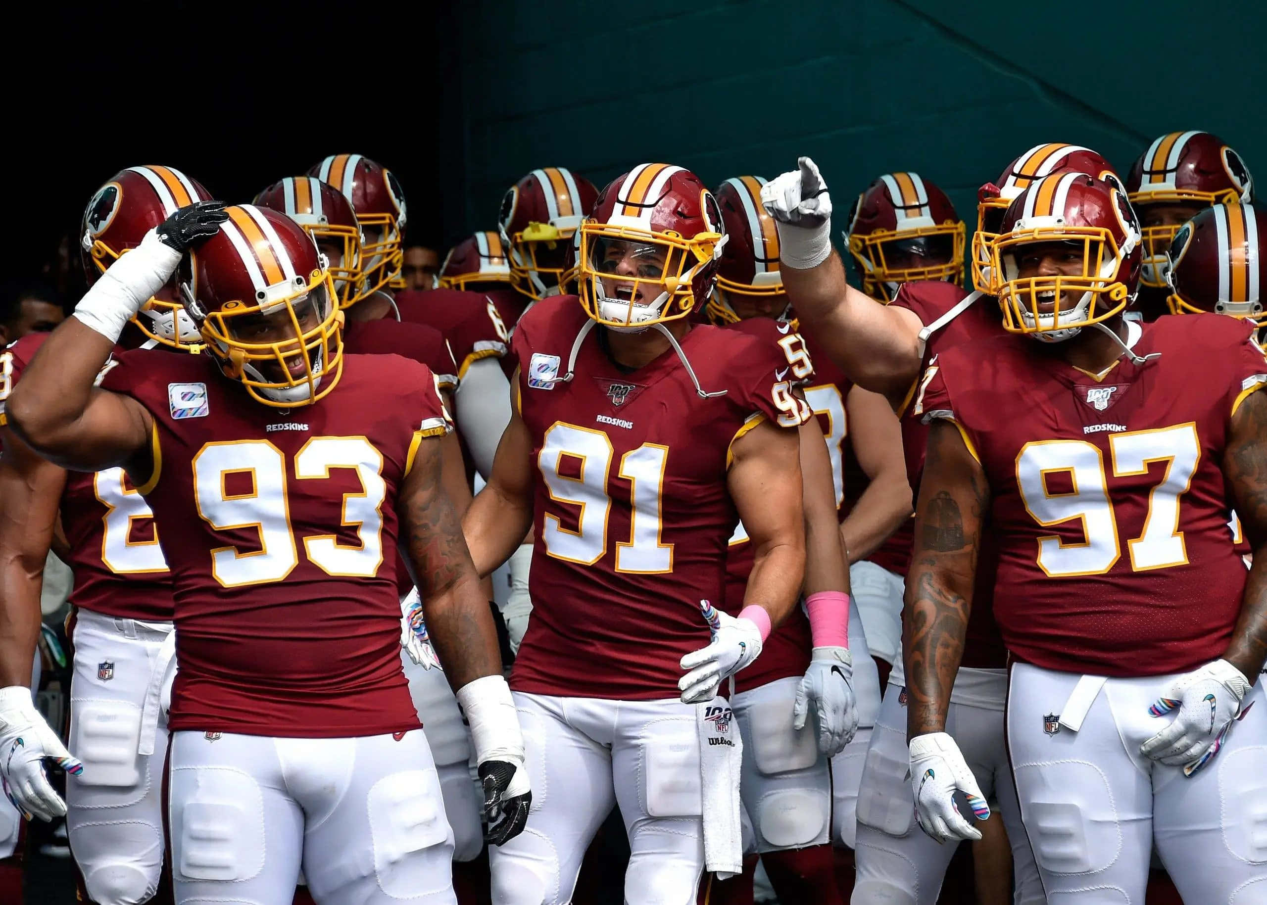Washington Football 桌布 壁紙 — 華盛頓美式足球隊球員身穿栗色和金色制服，在體育場燈光下的球場上列隊行走。