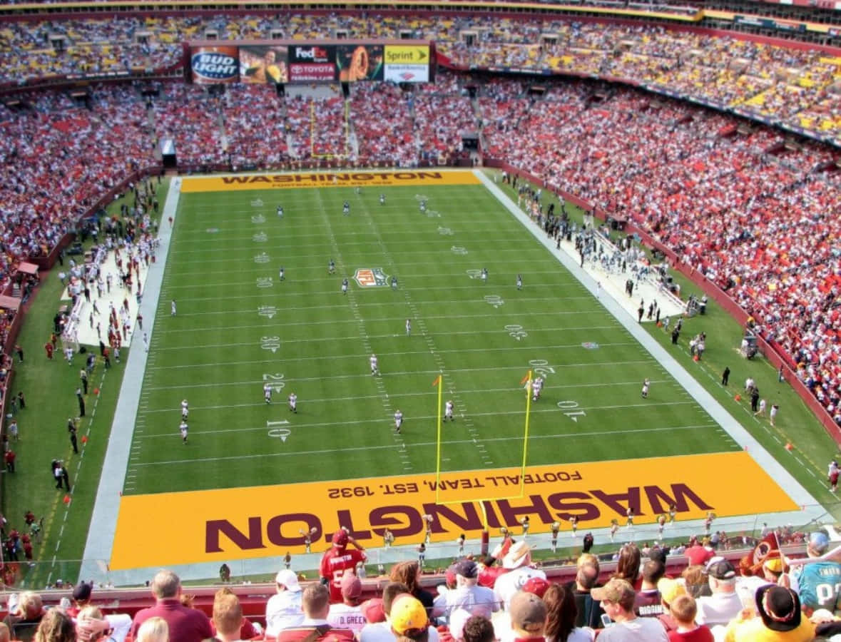 Washington Football 桌布 壁紙 — 華盛頓足球場的空中俯瞰圖，場內擠滿了球員和坐在紅色及金色座位上的球迷。