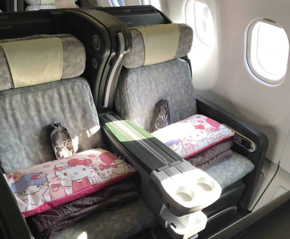 飛機商務艙座位上的Hello Kitty枕頭，陽光穿過窗戶。