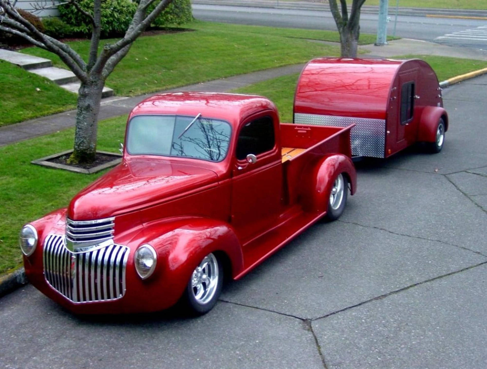 光澤的紅色經典卡車在潮濕的街道上拖著一輛紅色淚滴形拖車。