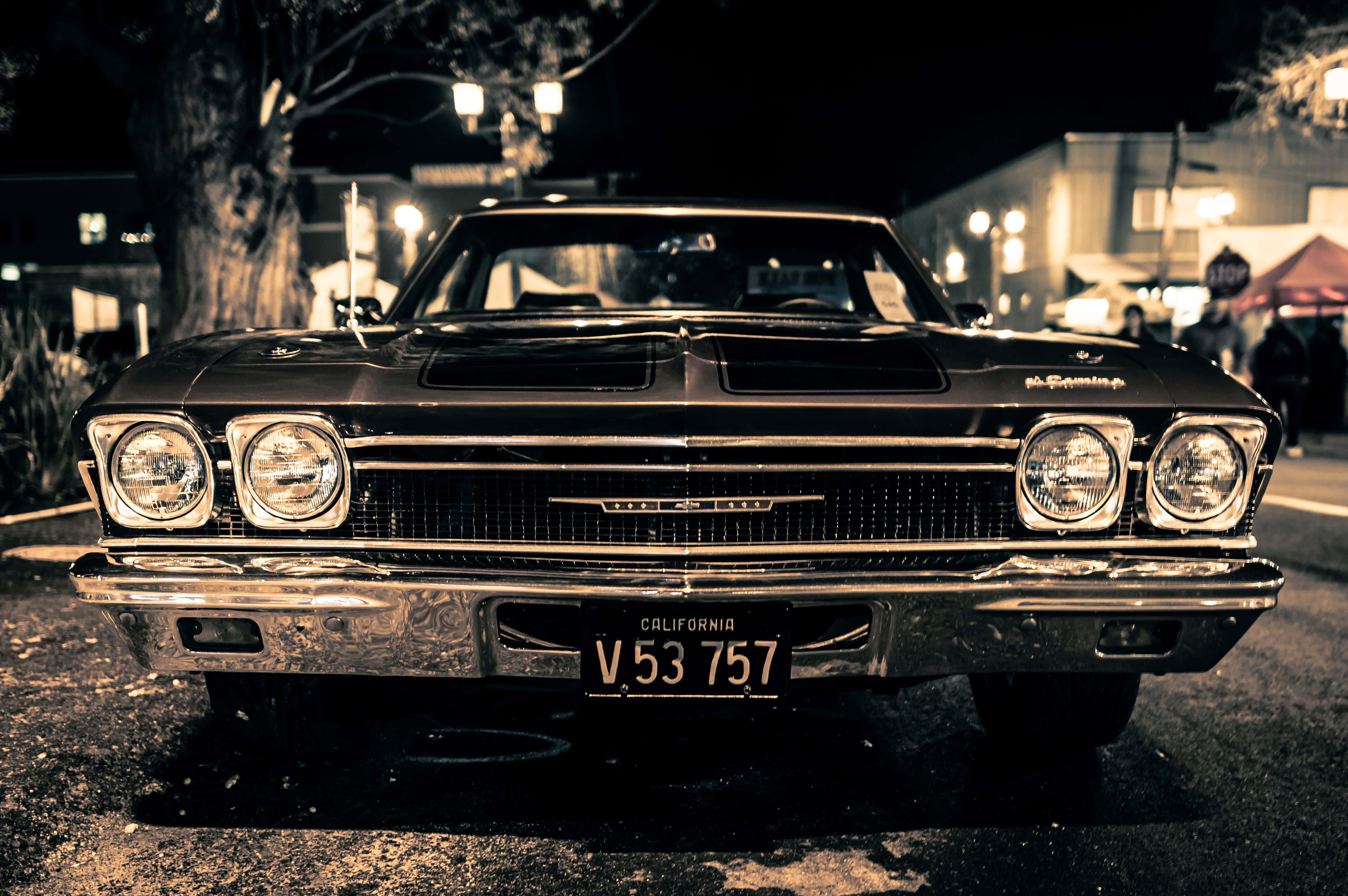 華麗經典雪佛蘭Impala——傳奇復古車款 壁紙 — 一輛帶有鍍鉻細節的復古黑色雪佛蘭在夜間潮濕的城市環境中，在街燈下閃閃發光。
