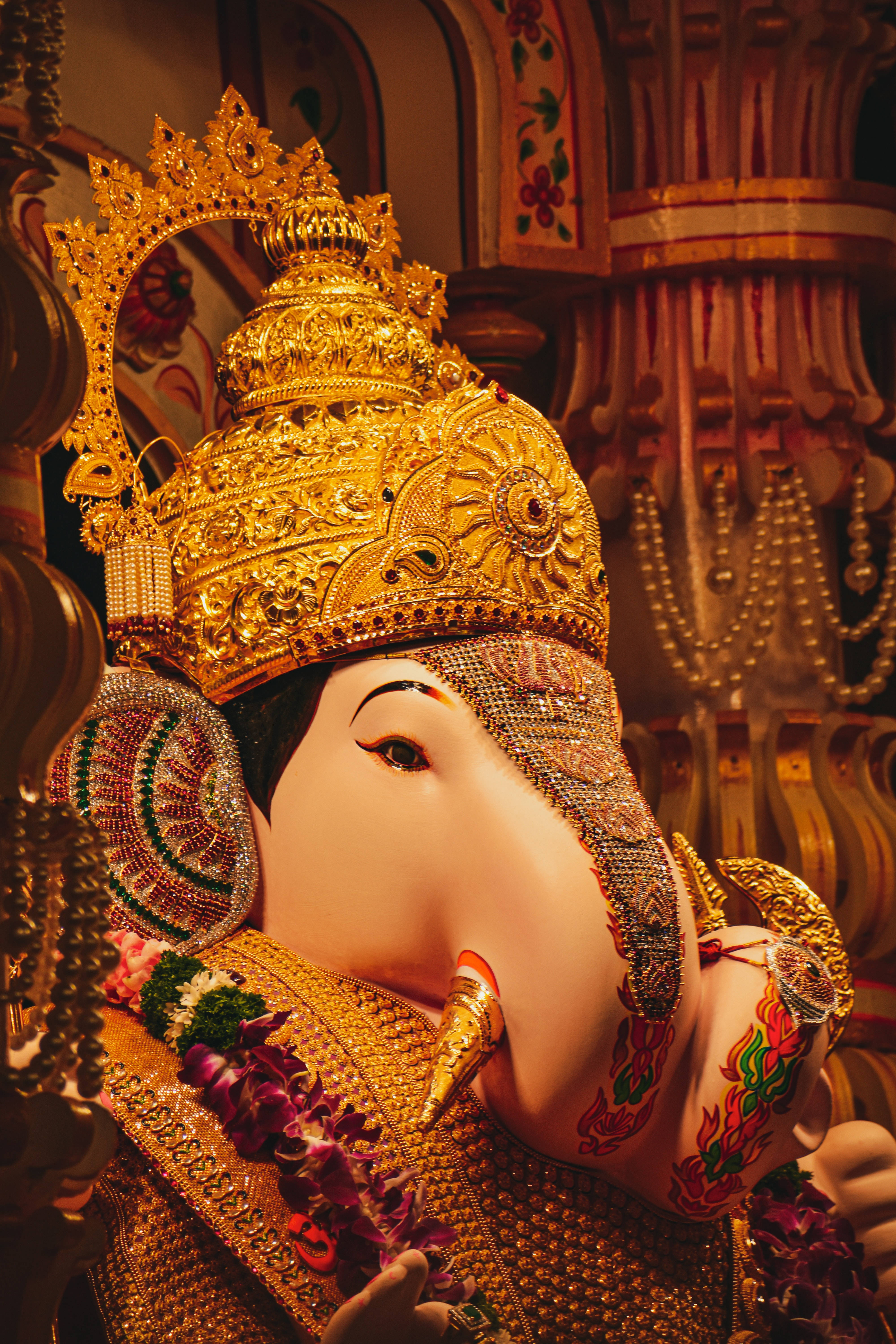 ganesh iPhone 桌布 壁紙 — 華麗金色象神雕像的特寫，飾有珠寶和花環，在溫暖的寺廟燈光下。