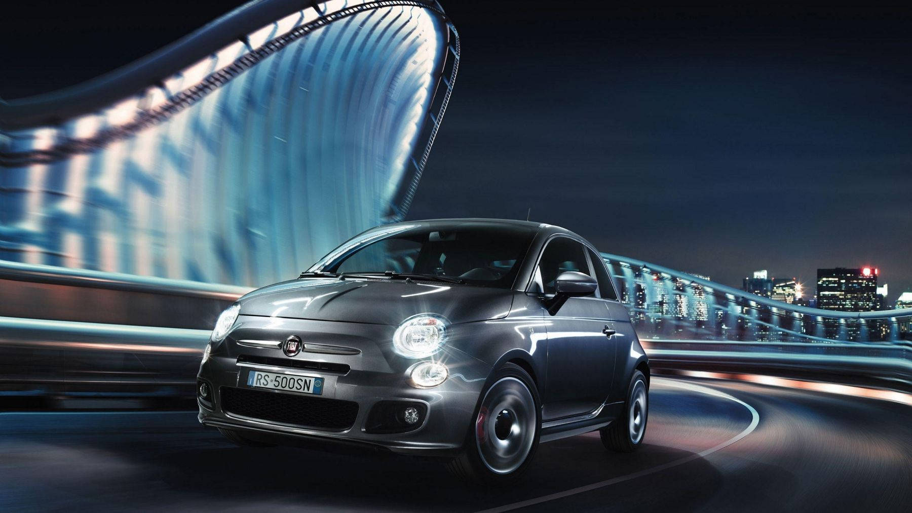 銀色Fiat 500S在夜間在彎曲的橋樑上飛馳，背景是城市燈光。