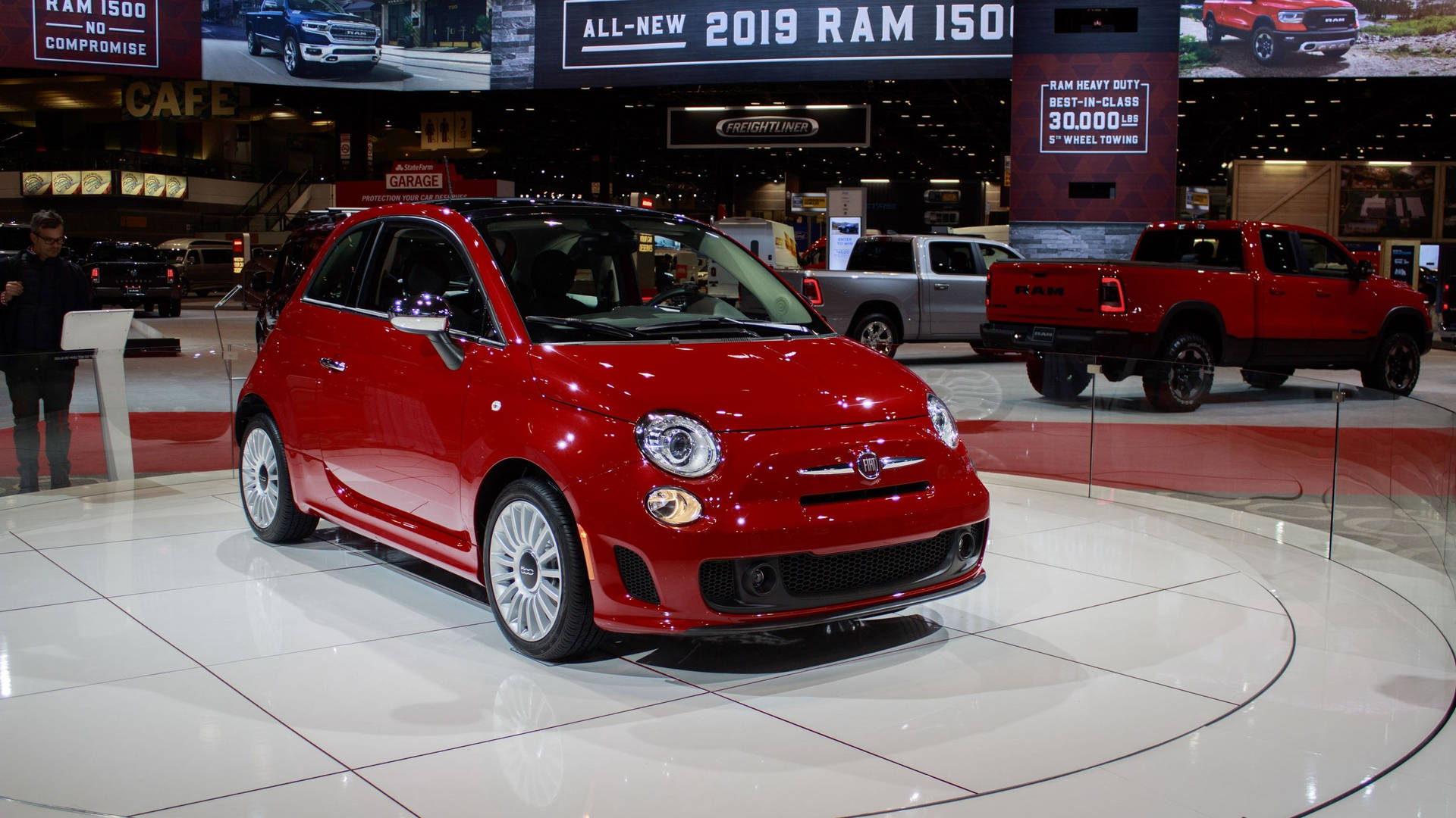 紅色Fiat 500汽車在展廳地板上展示，旁邊有其他車輛和標誌。