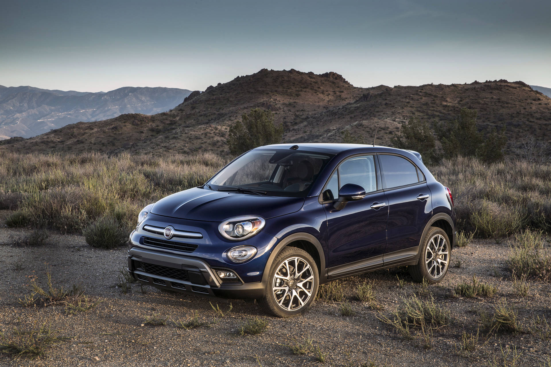 暮色中，乾燥丘陵景觀的碎石上停著藍色Fiat 500X SUV。