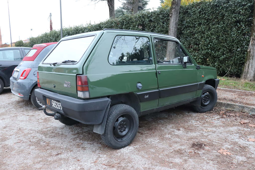 菲亞特車款代表義大利汽車設計巔峰 壁紙 — 一架復古綠色Fiat Panda 4x4停泊在碎石上，旁邊有樹籬，背景有樹木。