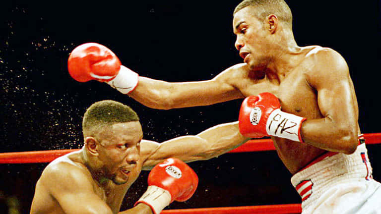 菲利克斯·特里尼達的強力重拳 壁紙 — 兩名拳擊手在雨水飛濺的擂台上交鋒，一人揮出紅色手套的一拳，另一人則準備迎接衝擊。