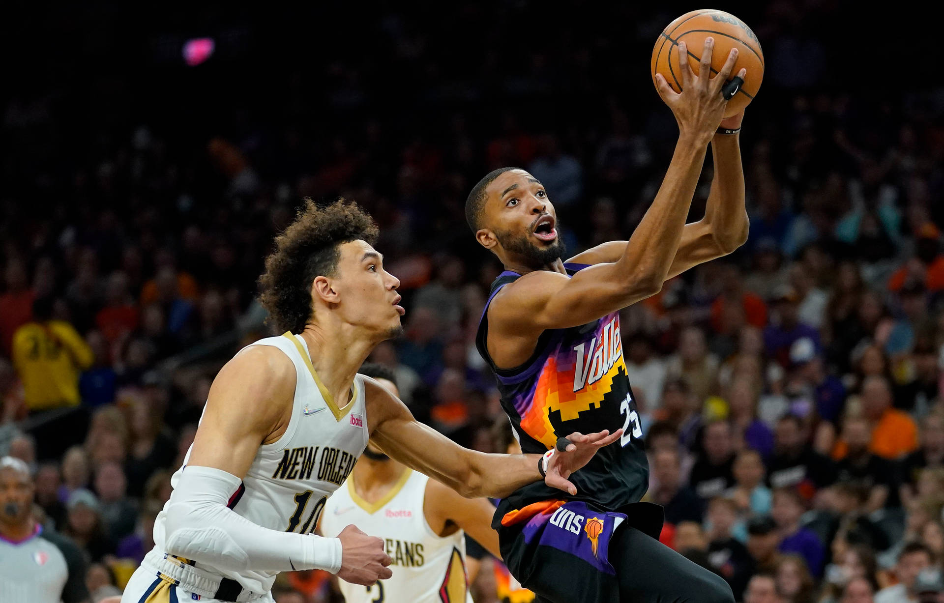 菲尼克斯對尼克斯 NBA 米卡爾·布里奇斯 壁紙 — 鳳凰城太陽隊球員跳起投籃，新奧爾良鵜鶘隊防守球員在座無虛席的球場上撲前封阻。