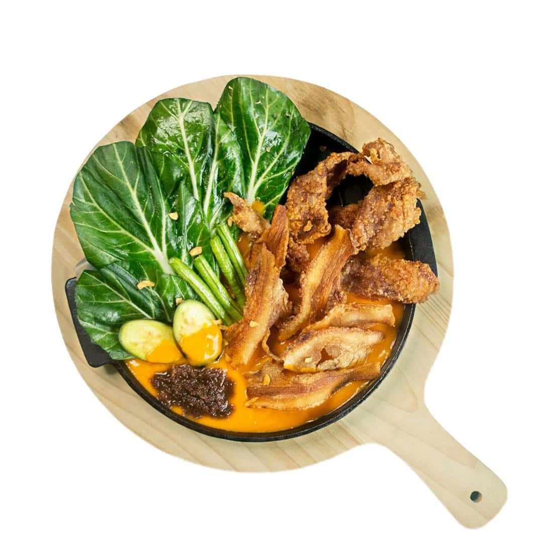 菲律賓名菜 Kare-Kare 的俯拍圖 壁紙 — 一個充滿活力的俯拍鏡頭，展示了一個鑄鐵煎鍋，裡面裝滿了酥脆的炸雞、小白菜、青豆和濃郁的橙色醬汁，放在木板上。
