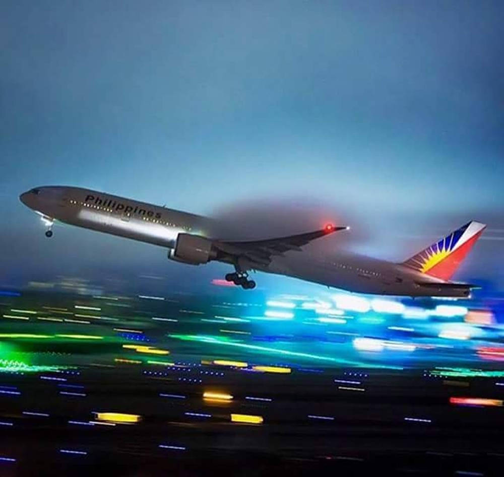 菲律賓航空飛機在夜間從發光的城市上空起飛。