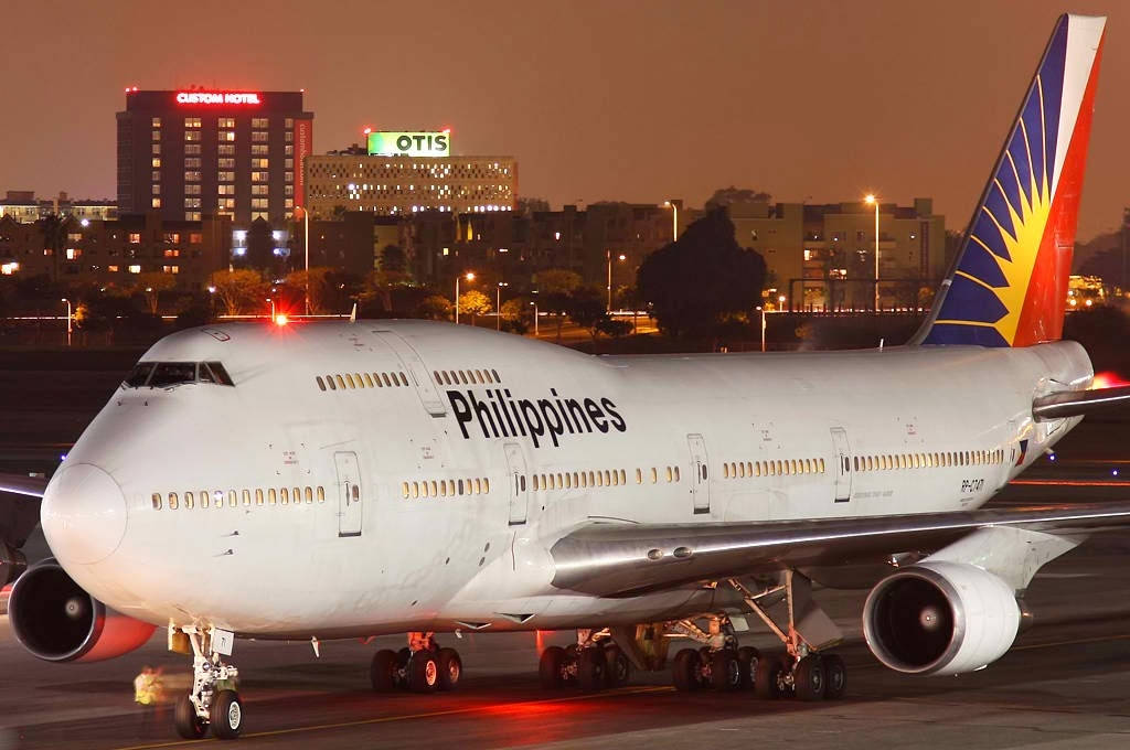 菲律賓航空珍寶客機夜間在停機坪，背後有城市燈光。