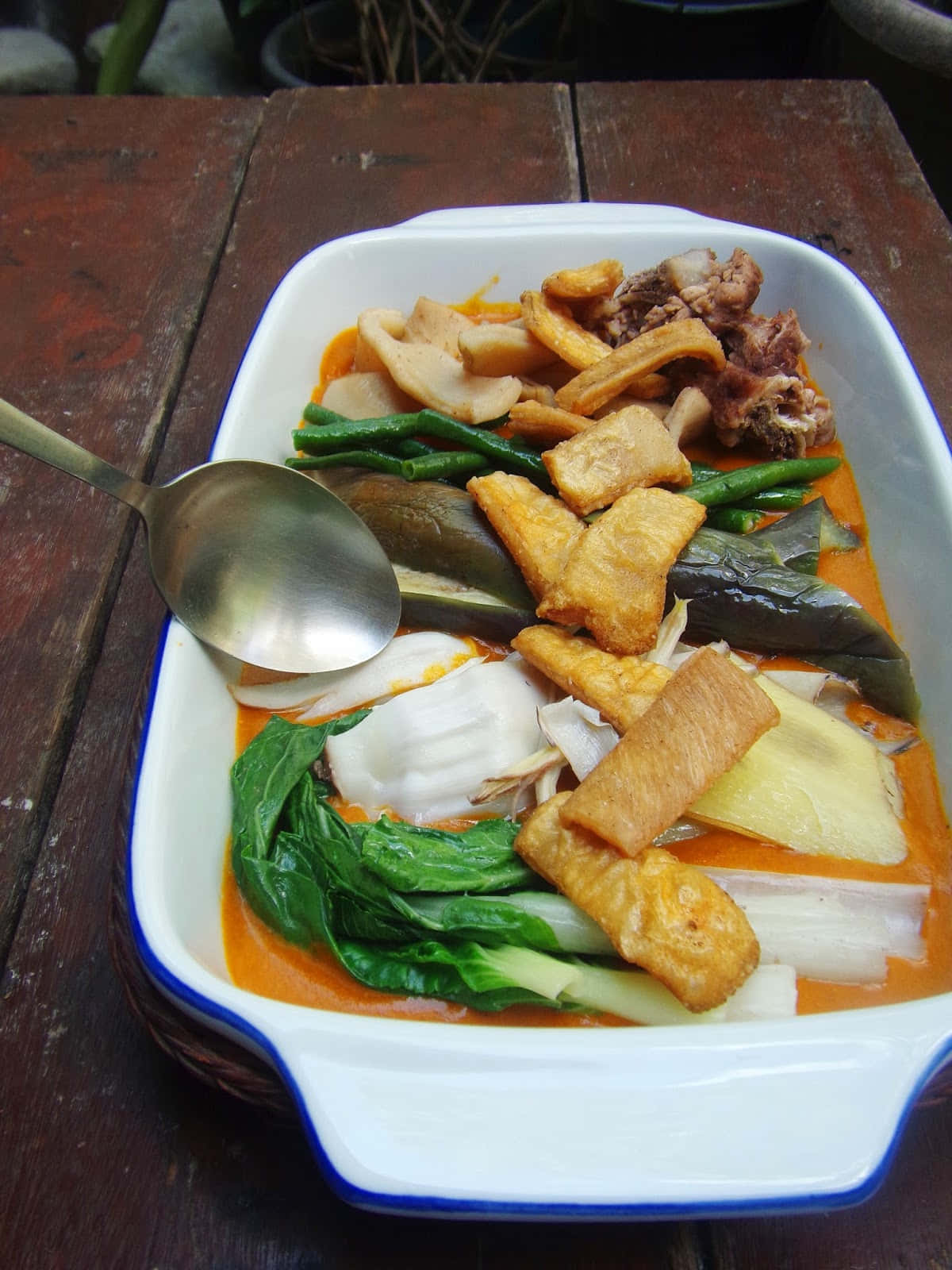 菲律賓菜式 Kare-Kare 盛宴 壁紙 — 一個冒著蒸氣嘅白色陶瓷碟，裝滿咗色彩鮮豔嘅橙色燉菜、豆腐同肉，放喺一張飽經風霜嘅木枱上面。