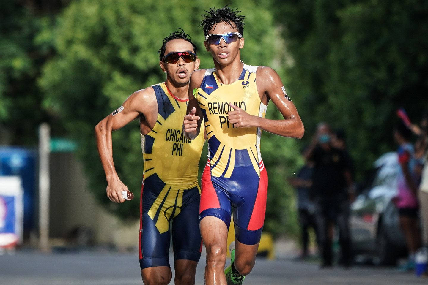 兩名男性鐵人三項運動員身穿黃、藍、紅色制服在街上比賽。