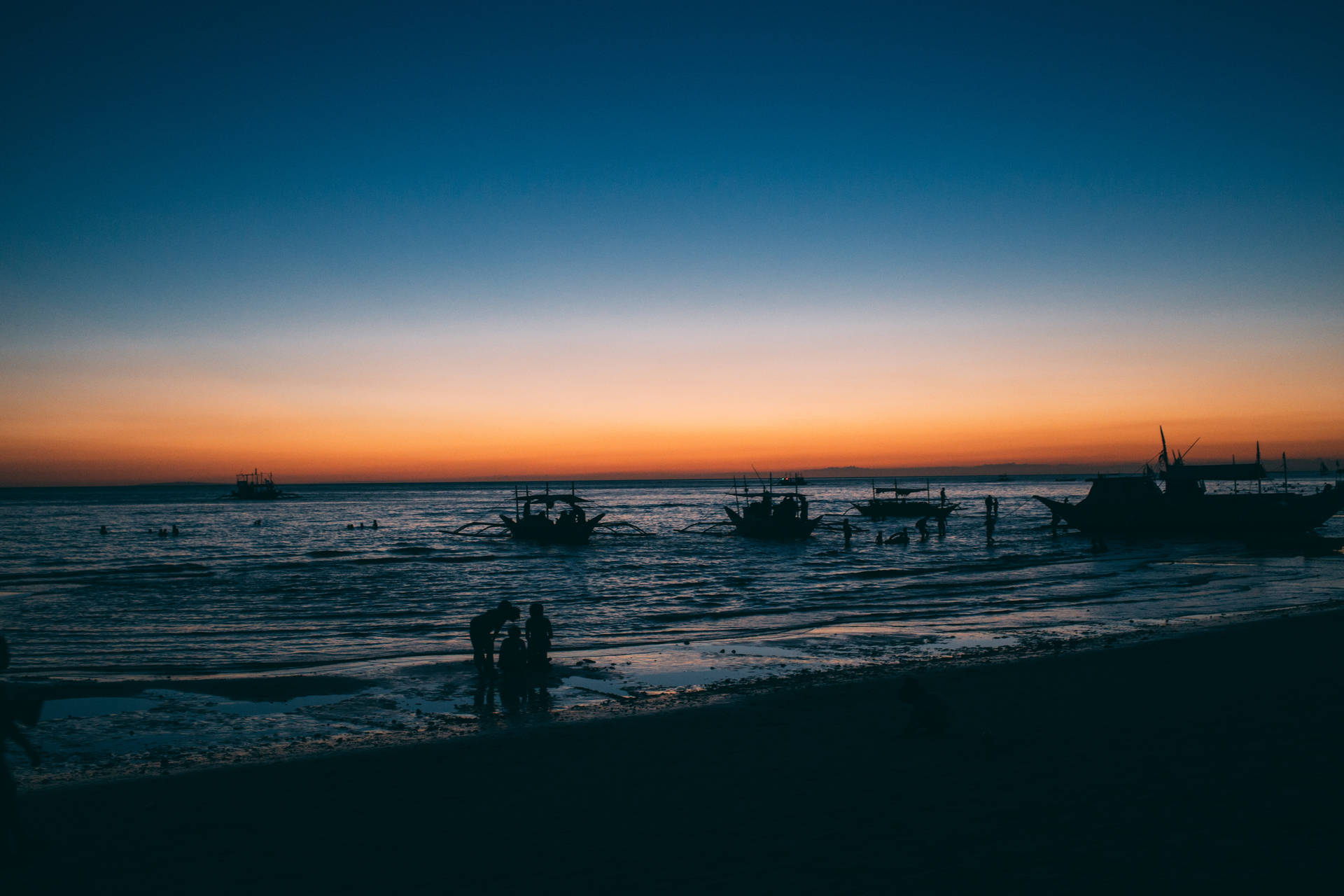 日落時分，海灘上船隻和人物的剪影，天空漸變色。