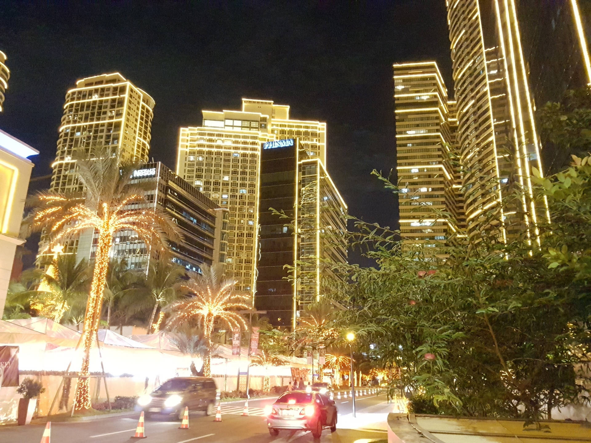 夜間城市景觀，有燈火通明的摩天大樓、棕櫚樹和交通。