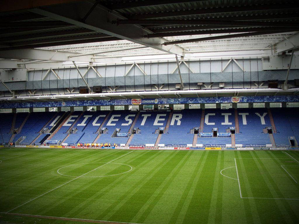 萊斯特城看台 壁紙 — 一個空無一人的足球場，藍色座位拼出「LEICESTER CITY」，俯瞰著充滿活力的綠色球場。