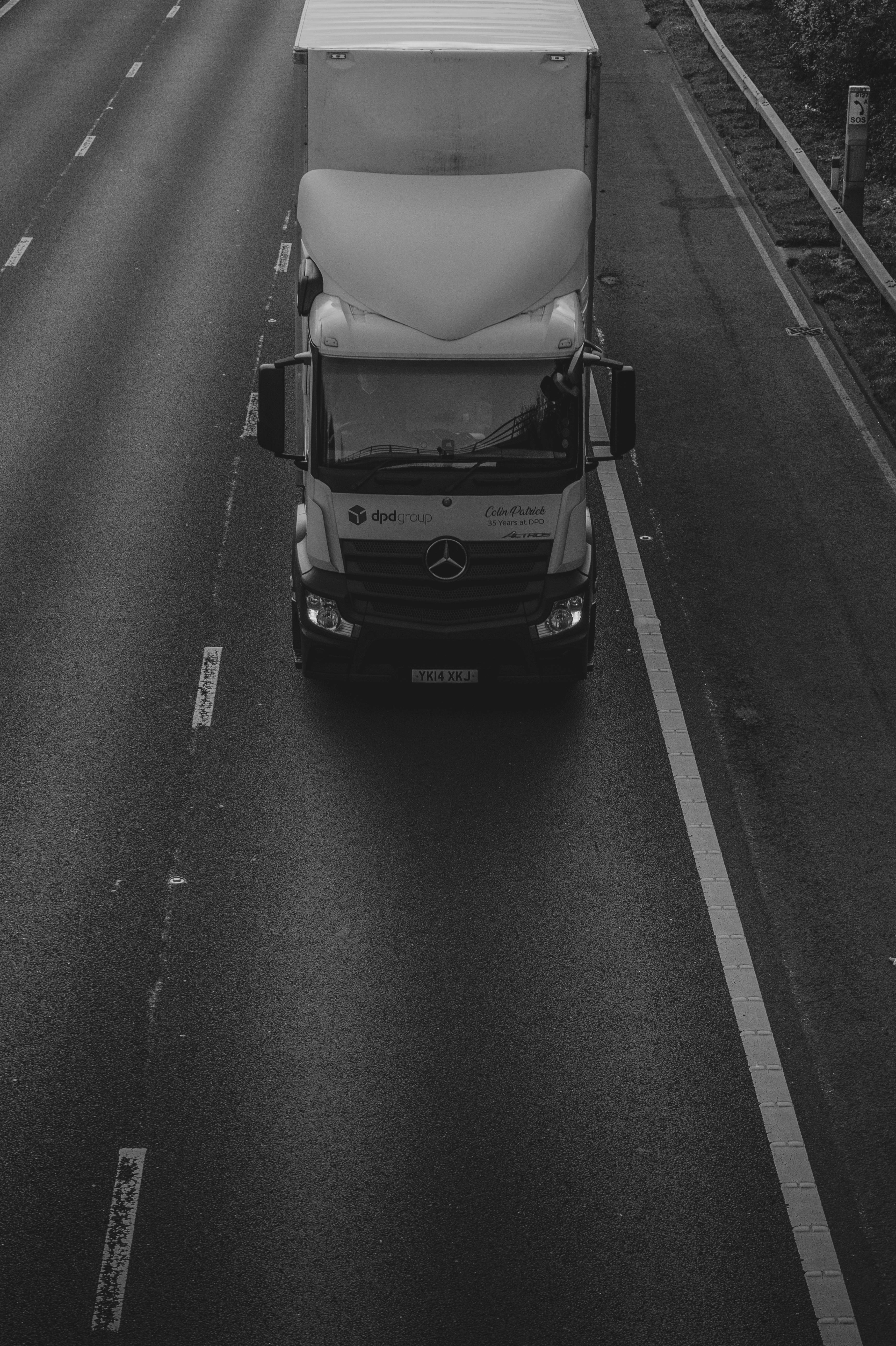 萊斯特郡高速公路上的貨車 壁紙 — 一張高角度黑白照片，拍攝一輛梅賽德斯-奔馳半掛卡車在潮濕的高速公路上行駛，車道標記清晰。
