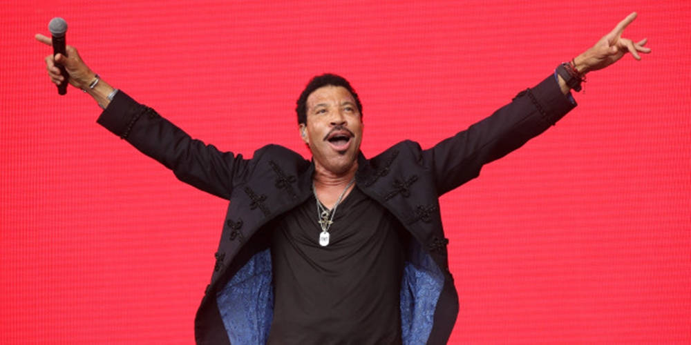Lionel Richie 在紅色舞台背景上舉臂歌唱。