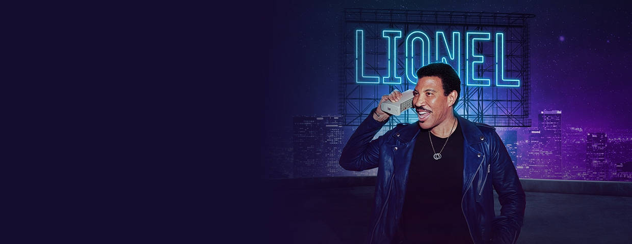 Lionel Richie 在天台上微笑，身後有霓虹燈標誌。