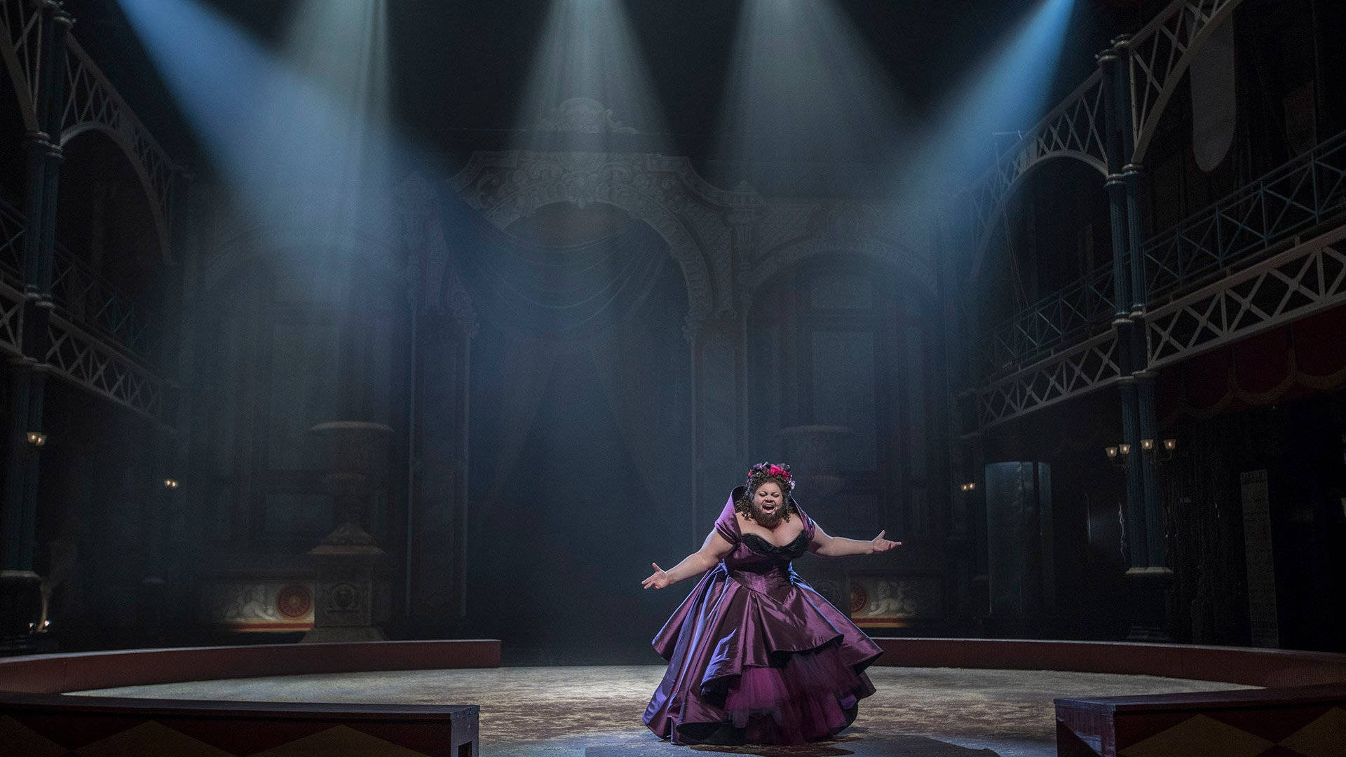 萊蒂·呂茲在《 Greatest Showman 》 壁紙 — 一位身穿紫色長裙的表演者站在華麗宏偉劇院的舞台中央，在戲劇性的聚光燈下。