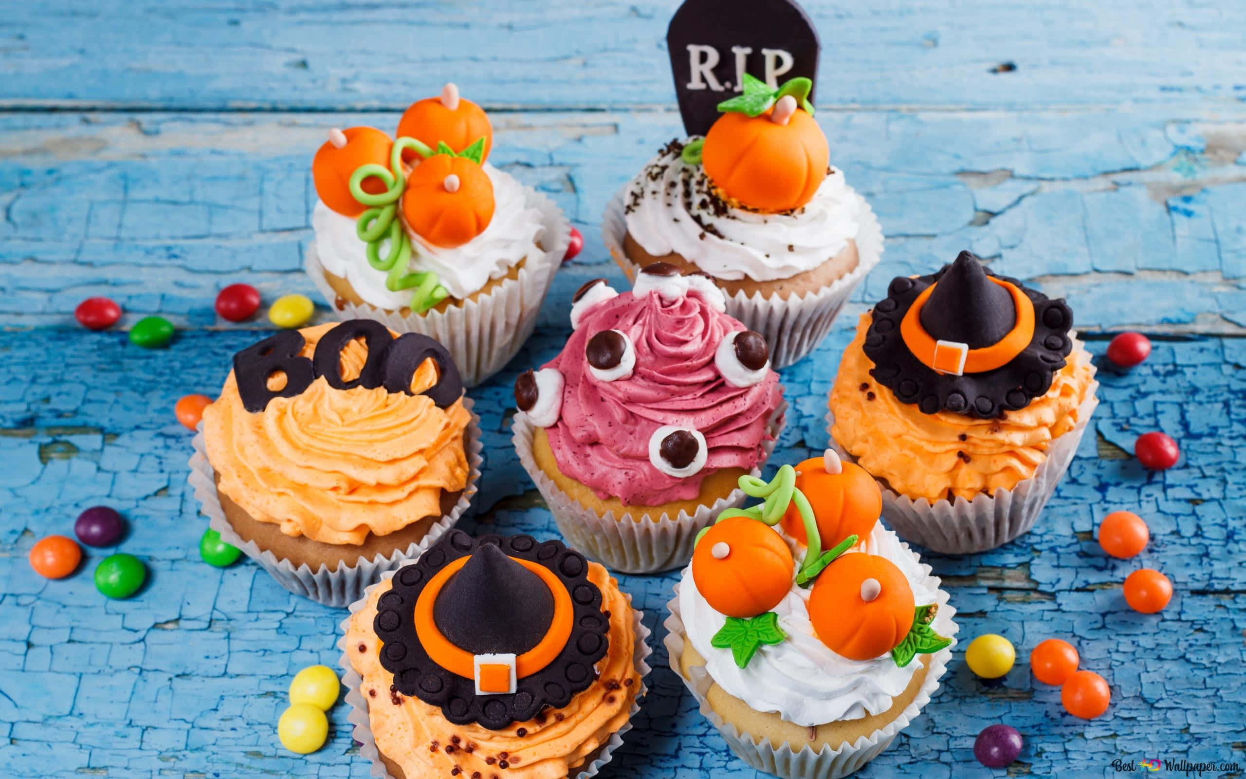Cute Cupcake 桌布 壁紙 — 萬聖節杯子蛋糕，裝飾著南瓜、巫婆帽和糖果，散落在風化的藍色木質表面上。