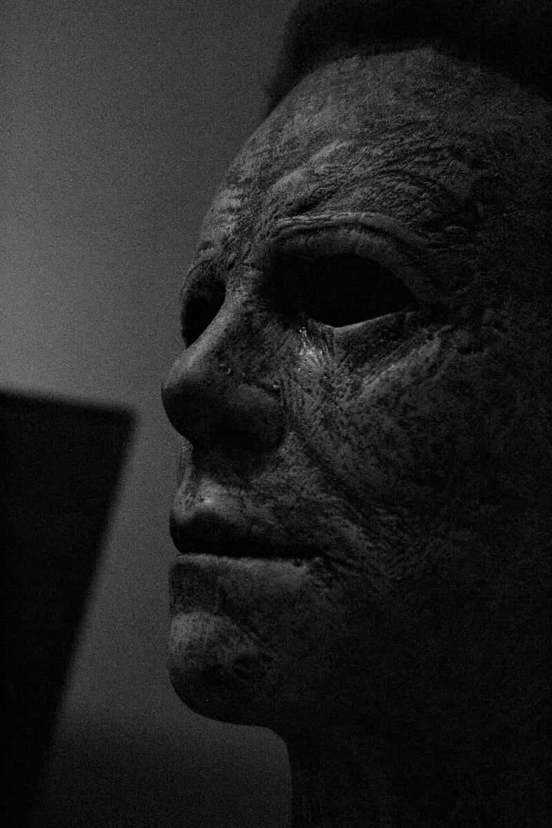 萬聖節邁克爾·邁爾斯威脅殺手 壁紙 — Michael Myers 標誌性傷痕面具在戲劇性側光下的黑白特寫，令人毛骨悚然。